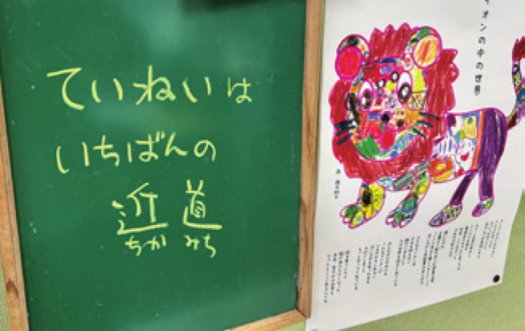 「ていねいはいちばんの近道」と書かれた黒板とライオンのアート作品